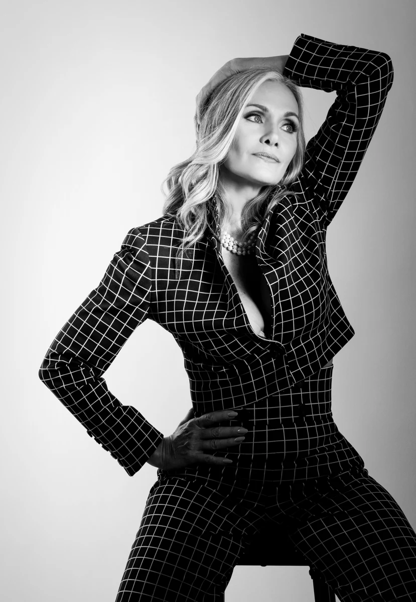 Retrato en blanco y negro con brazo sobre la cabeza y blusa a cuadros.